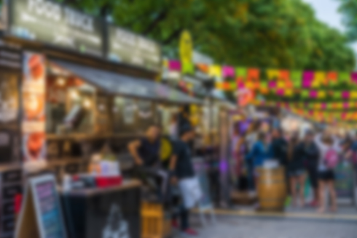 Food trucks and people at a street food market festival on a sunny day, blurred on purpose
